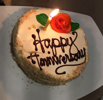 cake with Happy Anniversary on it, with an icing rose and a single candle